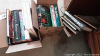 Two boxes filled with assorted flower and gardening books arranged vertically in cardboard boxes on a carpeted floor.