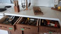 Overall view of kitchen counter with knife blocks, rotating utensil stand, and open drawers showing various kitchen tools.