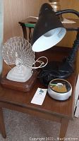 Clear acrylic peacock lamp, black desk lamp, and silver LED lamp on wooden side table.