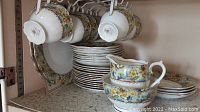 Photo of stacked plates with hanging teacups showing floral pattern and gold trim