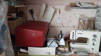 Overview of Bernina sewing machine, red carrying case and box of supplies on pegboard-backed worktable