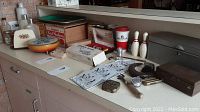 Wide view of tabletop displaying various vintage kitchen and household items including tins, bowling pins, metal boxes, and games.