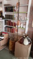 Full view of tension pole floor lamp with amber glass shades beside boxed chandelier shades and velvet shade lamp base
