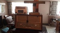 Wide shot showing General Electric bedside radio and desk lamp on wooden table with large Philips radio below