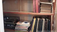 Photo of vintage vinyl records stacked on wooden shelving: albums include classical, opera, and other genres with visible titles on spines.