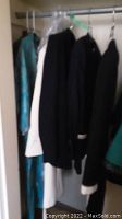 Photo showing several vintage women's clothing pieces hanging in a closet, including light blue and black garments.