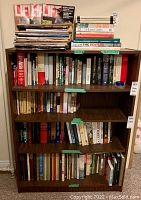 Photo of full bookcase with four shelves filled with various hardcover books and magazines visible on top shelf