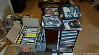 Photo showing boxes and stacks of assorted music CDs alongside the espresso wood CD holder.