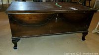Full front view of vintage cedar chest showing dark wood, carved decorative front panel, and cabriole legs.