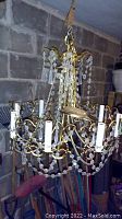 Overall view of brass chandelier hanging, showing multiple arms with candle style light sockets and crystal dangles.