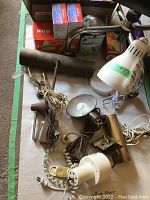 Photo showing multiple vintage desk lamps including brass lamps, a white clamp lamp, and a box with light bulbs on a beige surface.