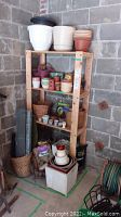 Full view of wooden shelving unit with upper shelves holding planters and pots in a concrete block wall garage corner