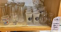Shelved glassware including shot glasses, clear glasses, frosted glasses, and small decanter style glasses