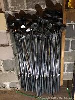 Full view of over five dozen golf clubs showing a mix of woods, irons and putters stacked upright.