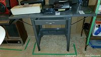 Metal drop leaf table viewed from front with drawer and shelf, some scratches visible