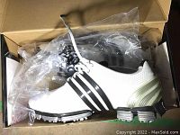 Side view of new Adidas golf shoe in box, white with black stripes