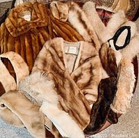 Vintage fur items including multiple fur stoles, collars, and a mink jacket arranged together on the floor.