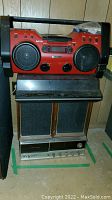 Photo showing the stacked stereo system with Panasonic controls, wooden cabinet speakers with black mesh, Hark Sound turntable on top, and a red Sony boombox on the very top.