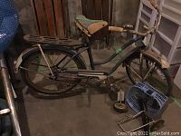 Side view of the vintage black bicycle showing frame, seat, handlebars, and basket with small extra wheels beside it.
