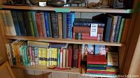 Two wooden shelves filled with a variety of vintage hardcover books, showing colorful dust jackets and spines of children's books and classic literature, including a small set of books with dark leather-like covers.