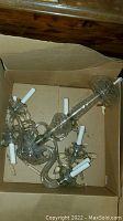 Chandelier packed inside a cardboard box showing the full piece with multiple arms and white candle bulb holders. Several cut crystal drops attached and one arm appears visibly broken.