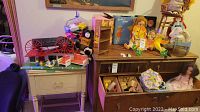 Wide view of the collection showing vintage Barbie doll cases, toys including a horse, and various dolls and accessories on furniture.