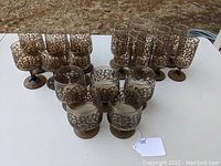 Overview of 19 Libbey Prado stemware glasses in tawny brown with scroll patterns, arranged by size groups on white table.
