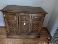 Closed vintage wooden bar cabinet with decorative carved front panels.