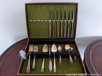 Open case showing all 46 pieces of silverplated flatware arranged in rows inside a wood box with green felt lining.