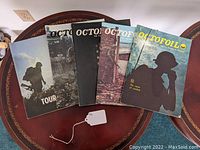 Five Vietnam War era army magazines displayed on round wooden table, including four issues of Octofoil and one Tour 365.