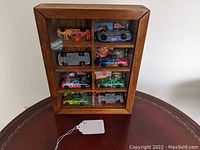 Front view of wooden display case holding 8 NASCAR diecast cars, arranged in 4 compartments, two cars each, with clear glass front.