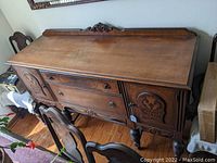 Full sideboard showing rectangular walnut top, ornate carved drawers, two carved doors, and turned legs.