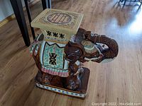 Side view of the Asian themed porcelain elephant garden stool showing detailed painted glaze designs and characters on the side with the trunk curled upward.