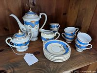 Full set arranged on wooden shelf showing coffee pot, creamer, sugar bowl, 6 cups, and 5 saucers.