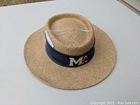 Front and side view of the natural straw Mickey Mouse hat showing the black band with an 'M' and an embroidered Mickey Mouse character.
