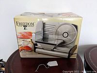 Photo of original retail box showing Freedom electric food slicer with plastic food carriage and circular blade on front side.