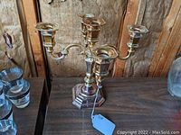 Front view of the silver plated four-arm candelabra on a wooden surface showing its structure, patina, and tag.