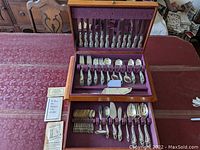 Wooden two-tier presentation case open, showing upper row of knives and lower row of forks, spoons, servers