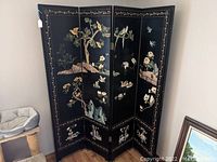 Full view of the 4-panel black lacquered privacy screen partially folded, showing bird and floral painted scenes with gold border detailing.