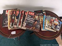Photo of a large group of magazines spread on two small tables. Shows multiple Life magazines, some Time and TV Guide issues, plus books and catalogs