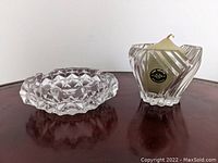 Clear glass ashtray with geometric pattern visible on top and side, shown on dark furniture surface