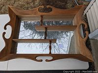 Wooden display shelf with mid-century colonial style frame, mirrored back, and three shelves placed on a white table outdoors.