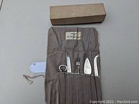 Full hors d'oeuvre utensil set arranged inside a beige fabric roll pouch with original cardboard box above.