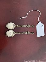 Pair of metal decorative spoons with ornate handles ending in mermaid figures, placed on dark background with a white tag labeled 40.