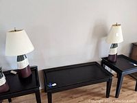 Pair of modern table lamps on black side tables against a white wall and wooden floor.
