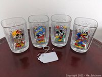 Four square-shaped drinking glasses with embossed Mickey Mouse head shapes and colorful character prints from year 2000 Millennium Disney Epcot Center series.