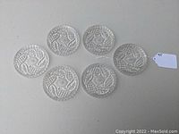 Top view of six clear glass drink coasters arranged on a table showing their embossed decorative surface pattern.