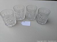Set of four clear heavy glass double old fashioned tumblers arranged on a white surface. Patterned base and thick walls visible.