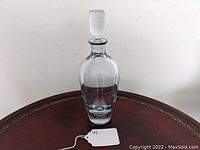 Full view of the sleek clear glass liquor decanter with stopper placed on a wooden surface.