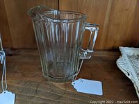 Clear vintage glass pitcher on wooden surface showing handle and pouring spout.
